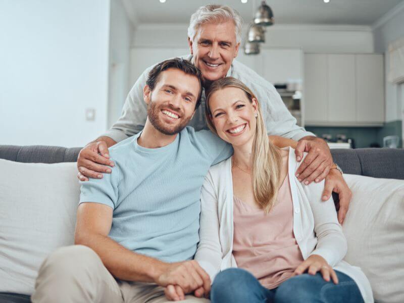 A cheerful elderly man stands behind a seated couple