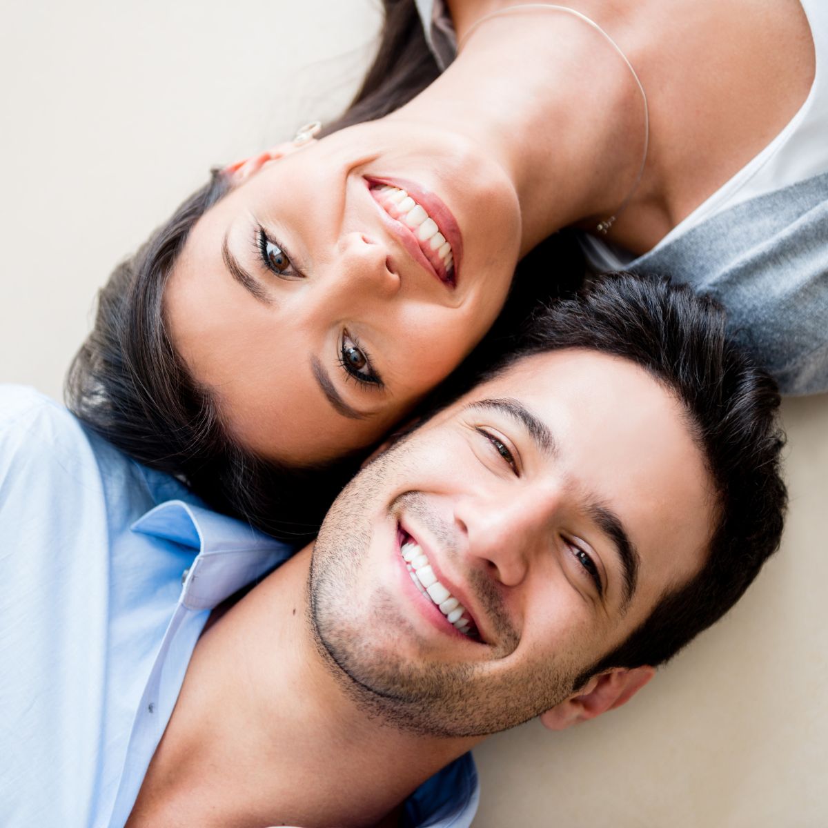 A man and woman share a joyful moment, smiling while lying on the floor, capturing a sense of happiness and relaxation.