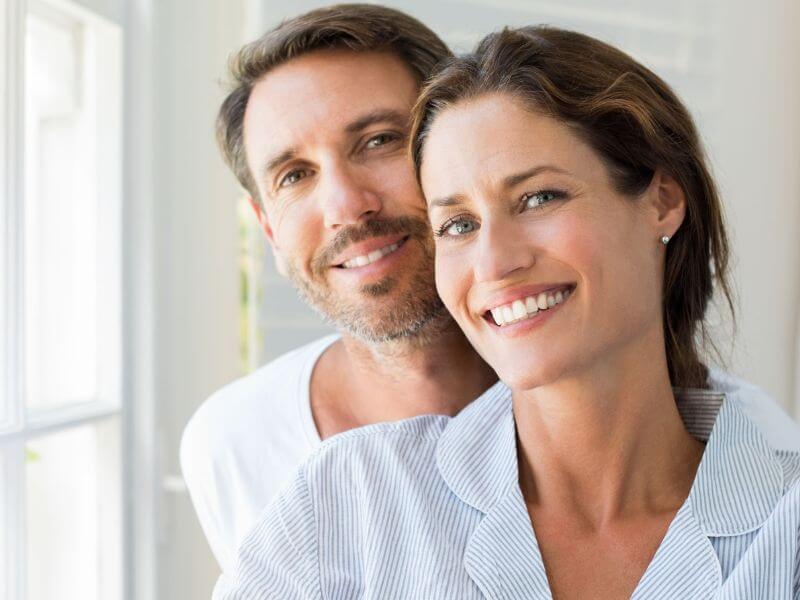 A smiling woman stands in front of a smiling man-tablet