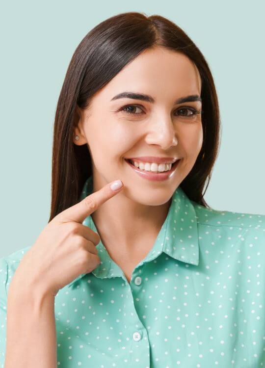 A woman smiles brightly while pointing to her teeth, showcasing her dental health and confidence.