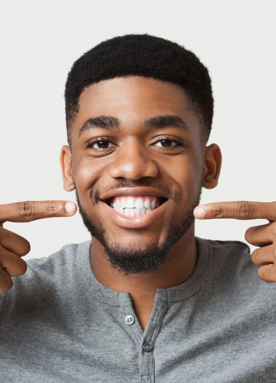 A man proudly displays his teeth by holding his fingers against his mouth, showcasing a bright smile