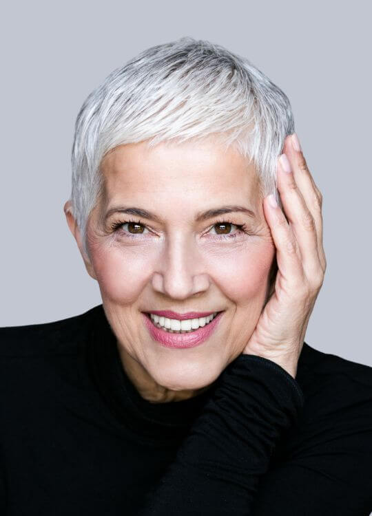  A woman with short white hair smiles warmly, exuding joy and confidence in her expression.