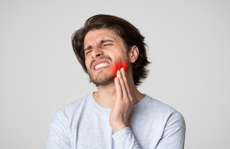 man grimaces in pain, holding his jaw