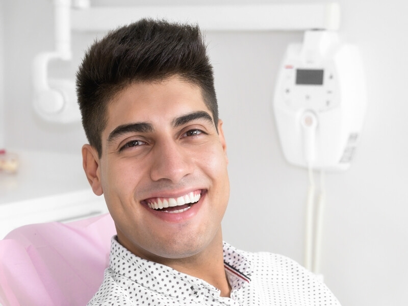 A man sits in a dentist chair while a dentist examines his teeth