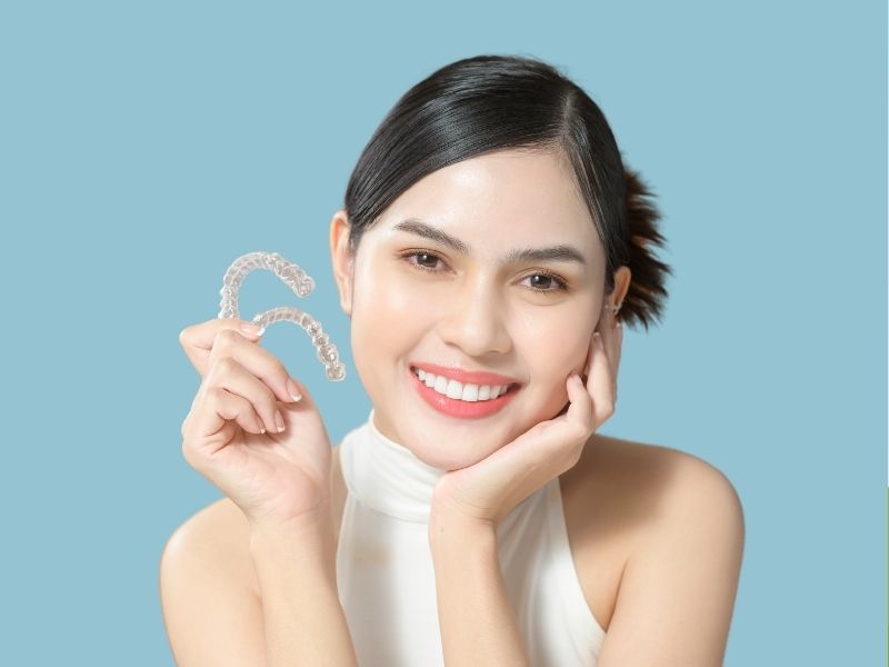 Women smiles while holding invisalign