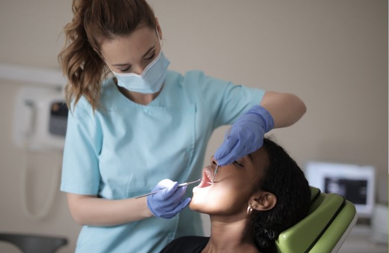  A woman sits in a dental chair as a dentist examines her teeth